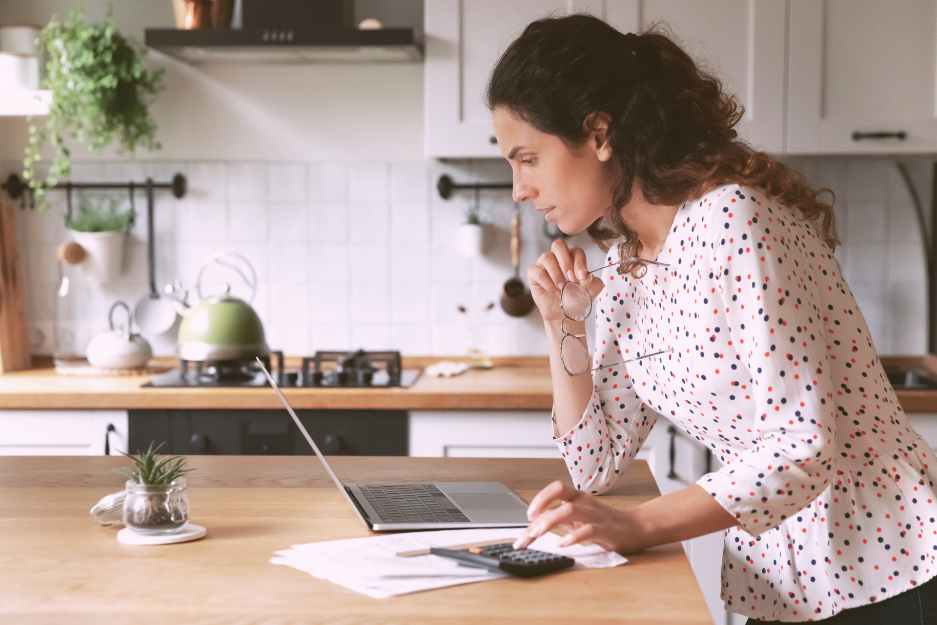 landscape images for web (13) woman in her kitchen with laptop working through life admin. Kettle in the background.