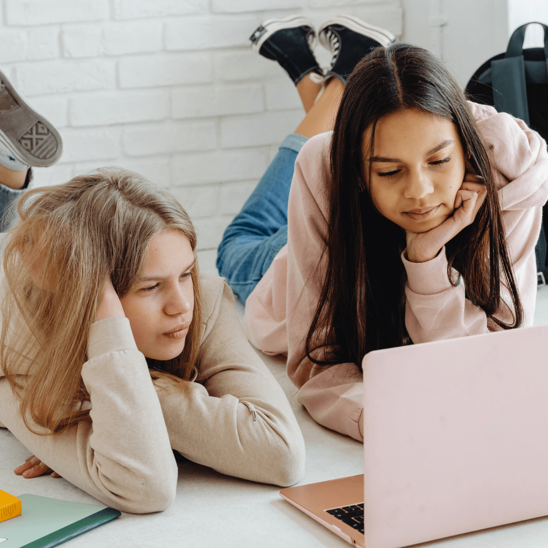 Teen girls lying on their fronts researching on a pink laptop